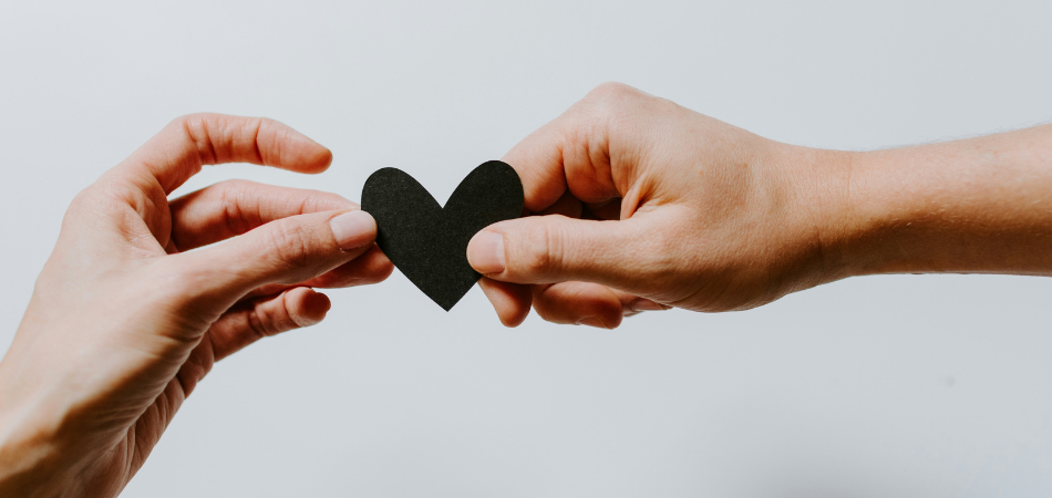 one hand giving another hand a black heart